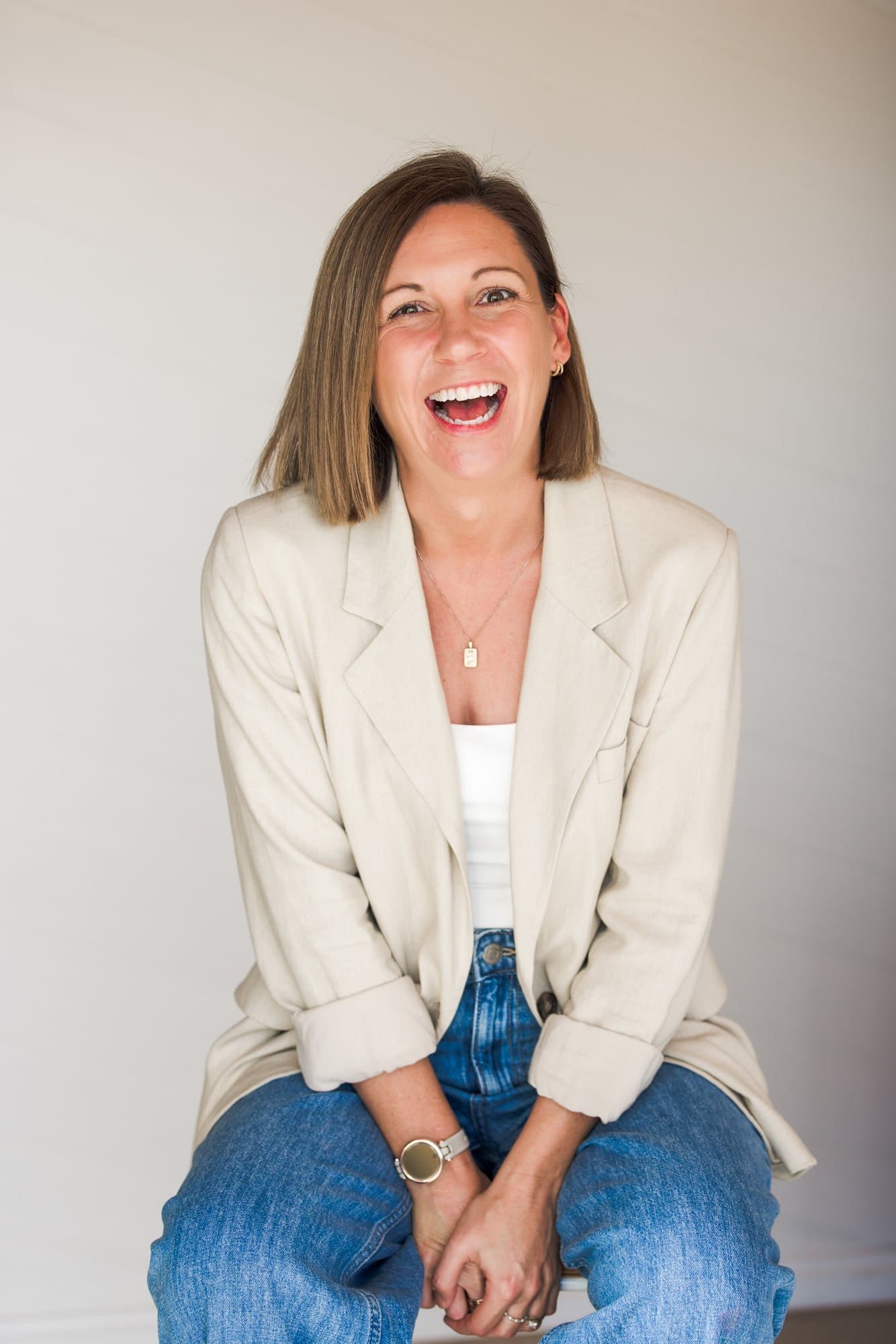 Steph seated in an oatmeal linen blazer, hands clasped, laughing straight at the camera